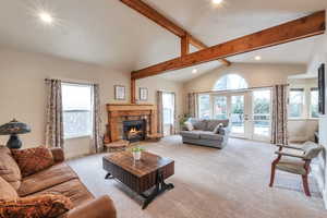 Living room featuring lofted ceiling with beams, a stone fireplace, light colored carpet, and a wealth of natural light