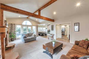 Living room featuring lofted ceiling with beams, a stone fireplace, and light carpet