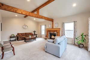 Living room featuring lofted ceiling with beams, a stone fireplace, and light carpet