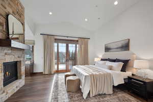 Bedroom featuring access to exterior, french doors, a stone fireplace, dark hardwood / wood-style flooring, and lofted ceiling