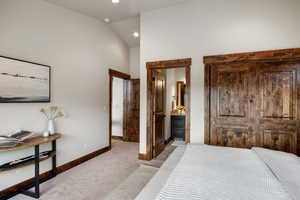 Carpeted bedroom with connected bathroom and high vaulted ceiling