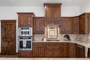 Kitchen with backsplash, stainless steel appliances, and light stone counters