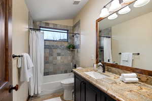 Full bathroom with vanity, toilet, shower / tub combo, and vaulted ceiling