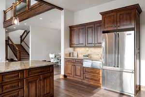 Kitchen featuring dark wood-type flooring, hanging light fixtures, decorative backsplash, high quality fridge, and light stone counters