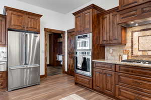 Kitchen featuring custom exhaust hood, light stone countertops, tasteful backsplash, light hardwood / wood-style floors, and stainless steel appliances