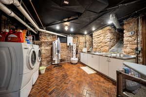 Clothes washing area with washing machine and dryer, tankless water heater, sink, and cabinets and walk-out basement entrance which is accessed from the rear/side yard.