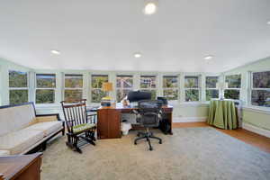 Windows surround this sun room family room/flex space with cork flooring.  Currently used as an office, but previously used as a family room.