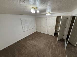 Unfurnished bedroom featuring dark carpet, a textured ceiling, and two closets