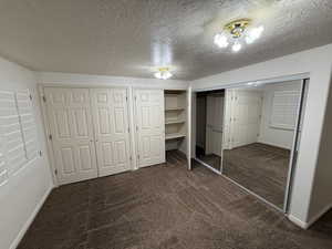 Unfurnished bedroom with dark carpet, a textured ceiling, and two closets