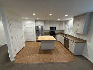 Kitchen featuring carpet flooring, sink, a center island, stainless steel appliances, and wood counters