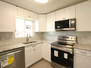 Kitchen with light stone countertops, tasteful backsplash, white cabinetry, appliances with stainless steel finishes, and sink