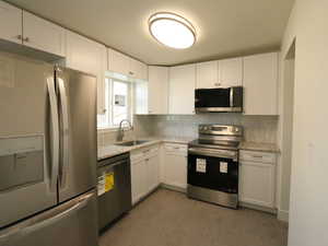 Kitchen with stainless steel appliances, sink, white cabinetry, light stone counters, and dark hardwood / wood-style floors