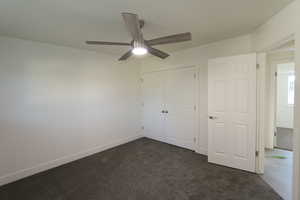 Unfurnished bedroom with ceiling fan, dark carpet, and a closet