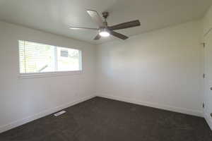 Spare room featuring ceiling fan and dark carpet