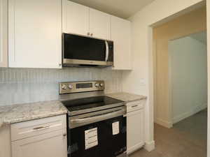 Kitchen featuring appliances with stainless steel finishes, light stone countertops, dark wood-type flooring, white cabinets, and backsplash