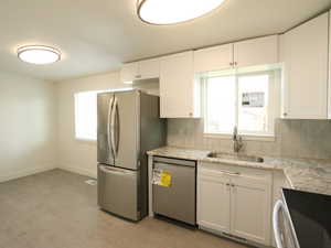 Kitchen with dishwashing machine, a healthy amount of sunlight, stainless steel refrigerator with ice dispenser, sink, and white cabinetry