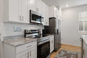 Kitchen featuring light stone counters, light hardwood / wood-style flooring, stainless steel appliances, and white cabinets