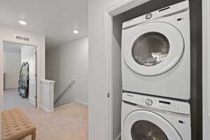 Laundry area featuring stacked washer / drying machine and light colored carpet