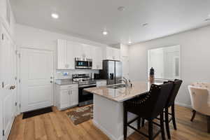 Kitchen with white cabinetry, an island with sink, sink, stainless steel appliances, and light stone countertops