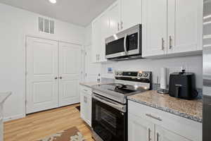 Kitchen with white cabinetry, appliances with stainless steel finishes, and light stone counters