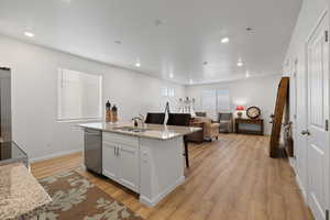 Kitchen with sink, light stone counters, a center island with sink, stainless steel dishwasher, and white cabinets