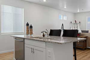 Kitchen featuring white cabinetry, sink, a kitchen breakfast bar, stainless steel dishwasher, and light stone counters