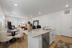 Kitchen with sink, dishwasher, light stone countertops, white cabinets, and a center island with sink