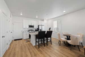 Kitchen with a breakfast bar, white cabinetry, light stone counters, an island with sink, and stainless steel appliances