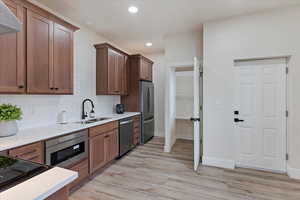 Kitchen with sink, wall chimney exhaust hood, tasteful backsplash, light hardwood / wood-style floors, and stainless steel appliances