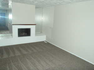 Unfurnished living room featuring a brick fireplace, a textured ceiling, and dark colored carpet