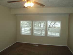 Spare room featuring dark colored carpet, a textured ceiling, and ceiling fan