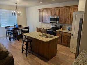 Kitchen featuring light stone countertops, appliances with stainless steel finishes, a notable chandelier, and sink