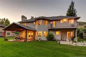 Back house at dusk with a patio, a balcony, and a lawn