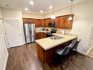 Kitchen with kitchen peninsula, appliances with stainless steel finishes, Knotty Alder Cabinets, LVP flooring and pendent lights