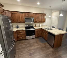 Kitchen with kitchen peninsula, appliances with stainless steel finishes, Knotty Alder Cabinets, LVP flooring and pendent lights