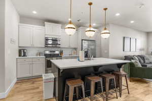 Kitchen featuring hanging light fixtures, backsplash, a breakfast bar area, a center island with sink, and appliances with stainless steel finishes