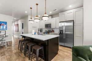 Kitchen featuring appliances with stainless steel finishes, a kitchen breakfast bar, a kitchen island with sink, white cabinetry, and hanging light fixtures