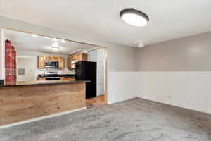 Kitchen featuring kitchen peninsula, carpet, dark stone counters, and appliances with stainless steel finishes