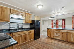 Kitchen with sink, backsplash, light hardwood / wood-style floors, a textured ceiling, and black refrigerator