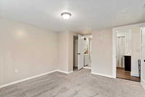 Unfurnished bedroom featuring light carpet, independent washer and dryer, a textured ceiling, and a closet