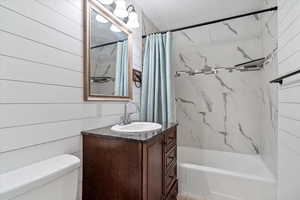 Full bathroom with vanity, wooden walls, toilet, a textured ceiling, and shower / tub combo with curtain