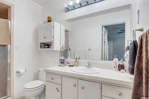 Bathroom with an enclosed shower, vanity, ceiling fan, and toilet