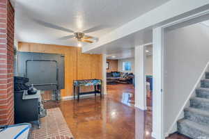 Rec room with a wood stove, wood walls, ceiling fan, and a textured ceiling