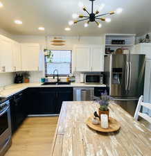 Kitchen with white cabinets, stainless steel appliances, a notable chandelier, decorative backsplash, and sink