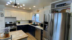 Kitchen featuring decorative backsplash, appliances with stainless steel finishes, sink, an inviting chandelier, and white cabinets