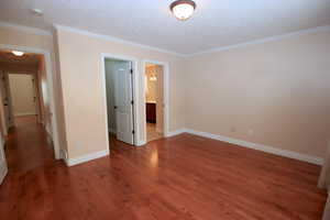 Primary Bedroom with walk in closet and ensuite bathroom featuring dark hardwood / wood-style flooring and ornamental molding