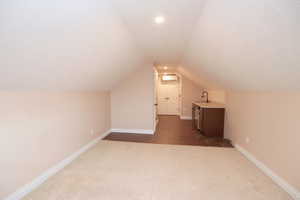 Bonus room featuring a wall mounted air conditioner, a textured ceiling, sink, carpet floors, and lofted ceiling