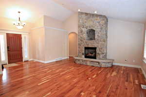 Unfurnished living room with hardwood / wood-style flooring, vaulted ceiling, and a notable chandelier