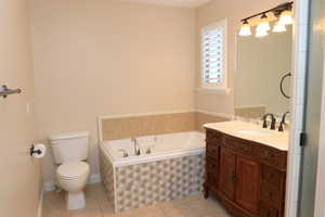 Primary ensuite bathroom featuring tiled bath, tile patterned flooring, vanity, and toilet, as well as separate tub and shower