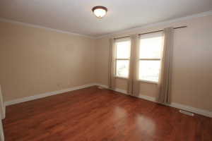 Primary bedroom featuring crown molding and dark wood-type flooring